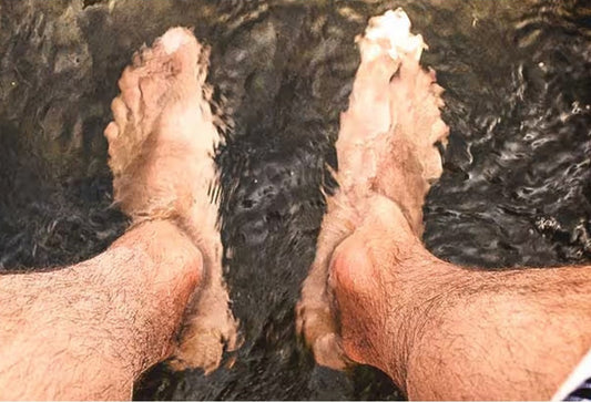 Bare feet and ankles submerged in a dark ionic foot detox bath, seen from the user's point of view