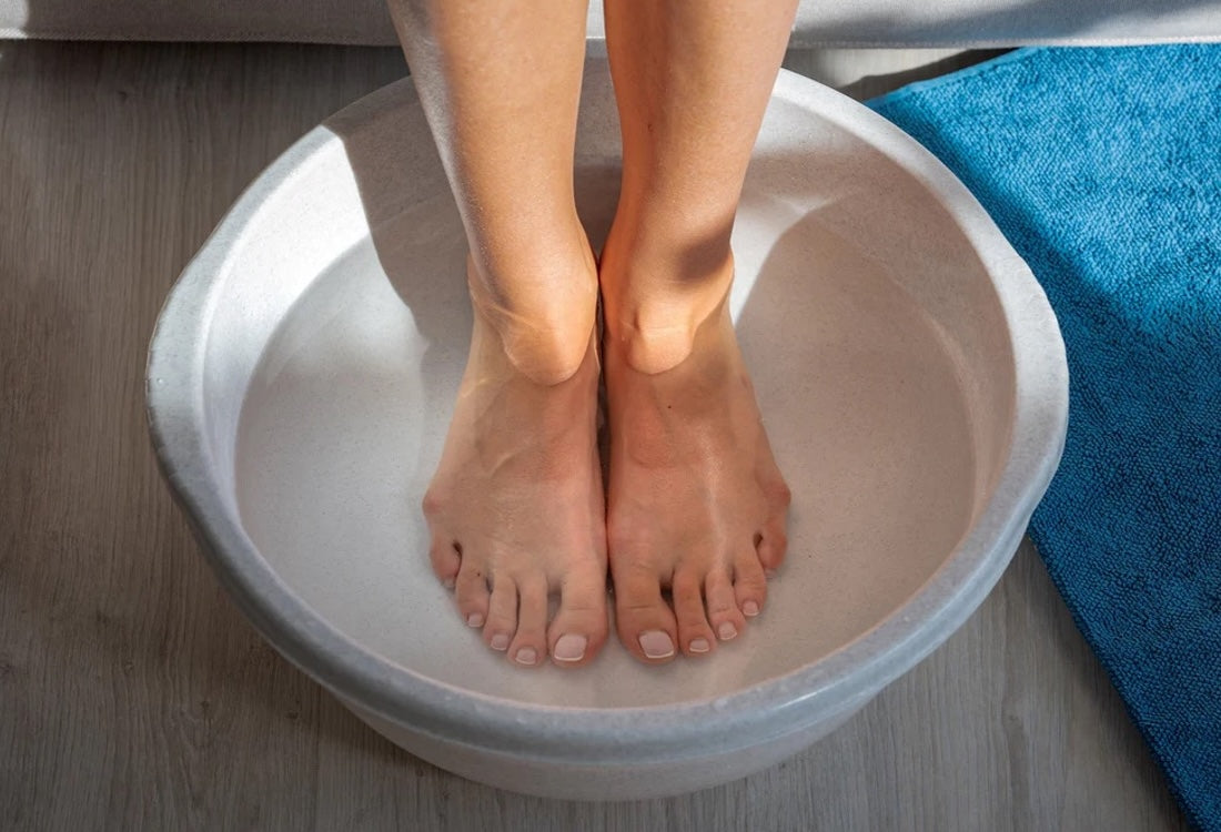 Bare feet submerged in a round silver basin during an at-home ionic foot bath detox session