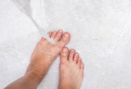 Bare feet under flowing water on a textured bath mat during an at-home ionic foot detox session