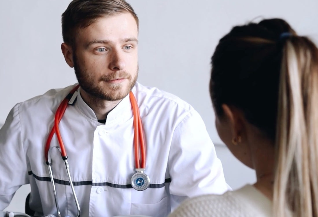 Male doctor in white coat with orange stethoscope listens attentively to a female patient during consultation