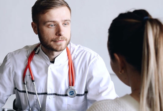 Male doctor in white coat with orange stethoscope listens attentively to a female patient during consultation