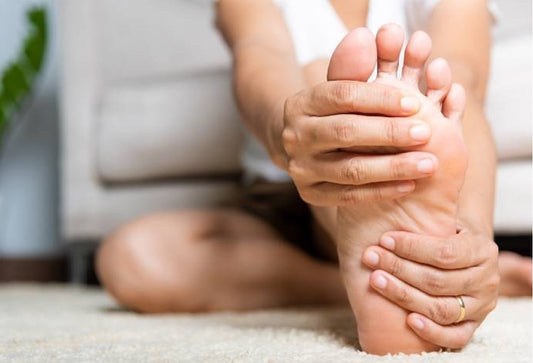 Person sitting cross-legged on carpet, gripping the sole of their foot to soothe tingling discomfort.